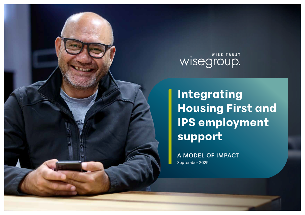 Report cover, photo of a man wearing glasses and a blue jacket, smiling and holding a mobile phone in front of him. The main title of the report is: Integrating Housing First and IPS employment support.